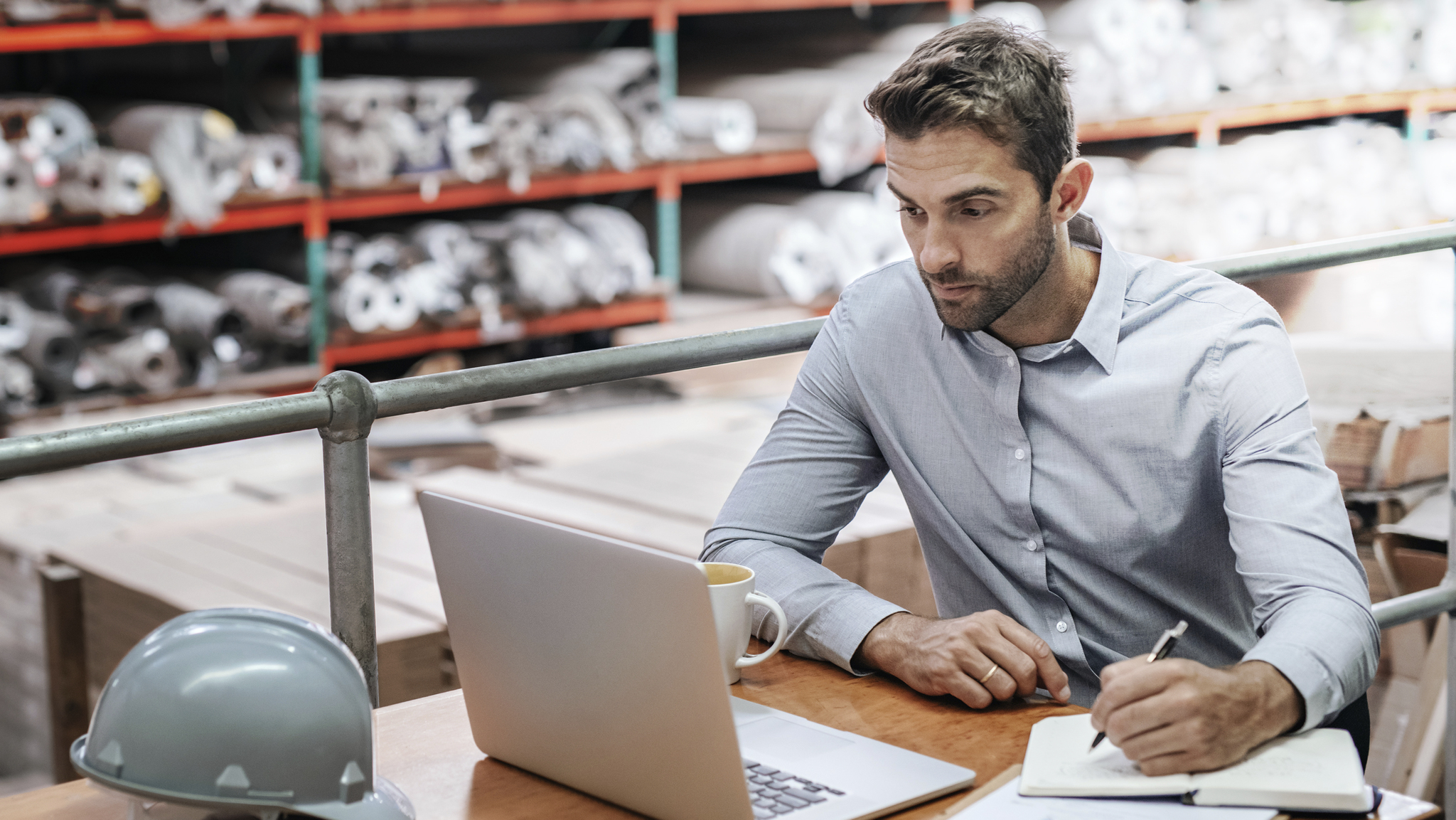 man in button up shirt working in warehouse looking at laptop