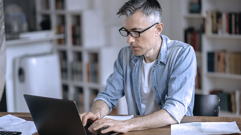 man in glasses working on laptop in home office