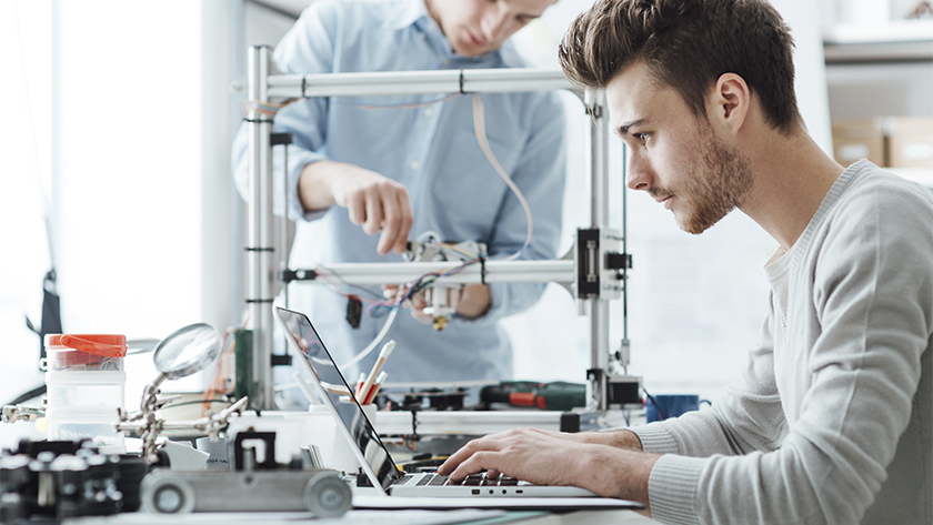 man in white sweater working on laptop in his workshop