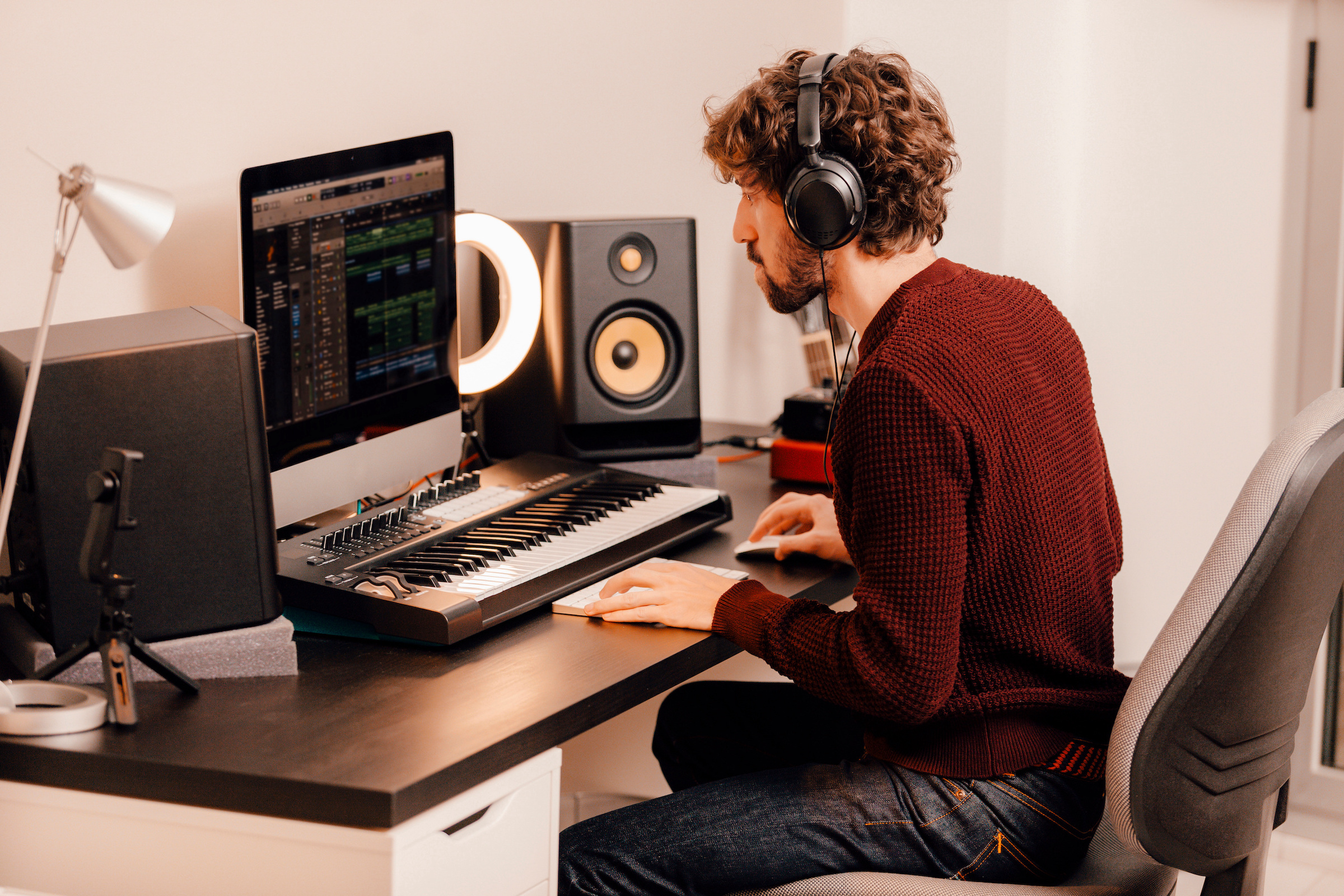 A man wearing headphones uses music software o a desktop computer. 