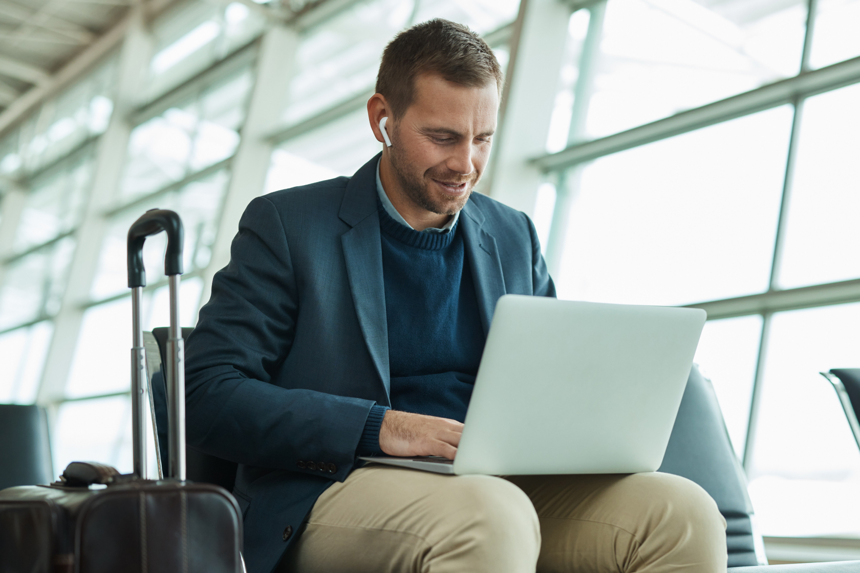A man works on his laptop in an airport while waiting for his flight to board. In order to legally deduct business travel, specific criteria must be met.