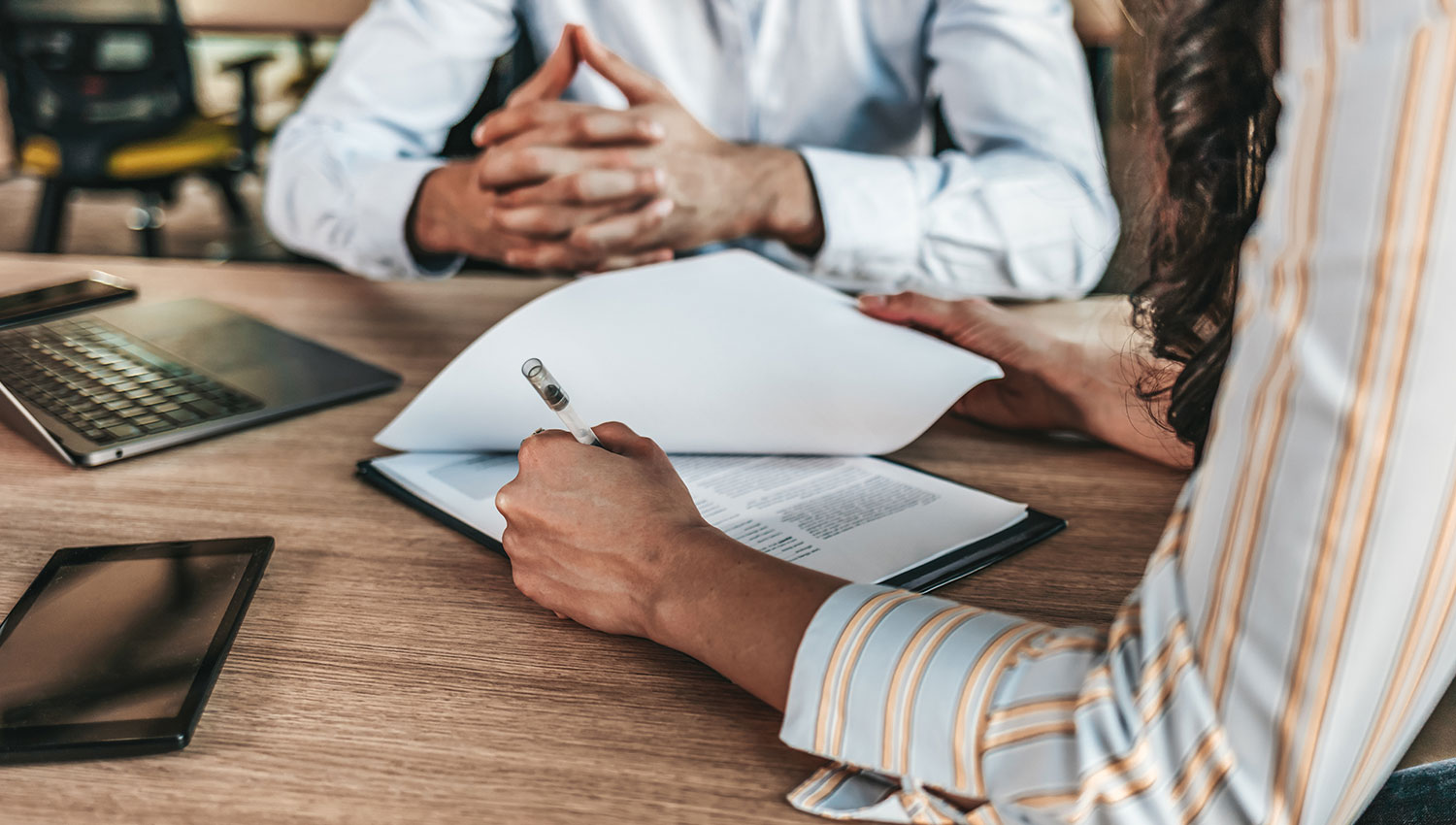 A person signs papers while someone else looks on. A release of liability form is designed to safeguard you against lawsuits by planning for and addressing potential disputes.