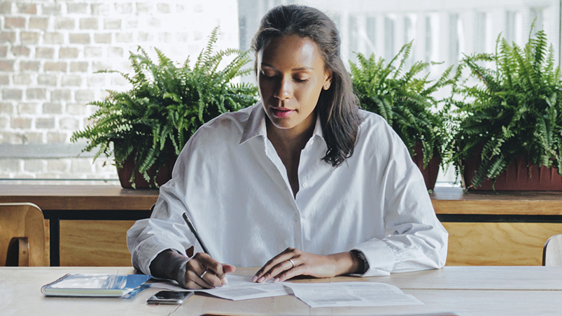 woman in button up shirt doing paperwork at her desk