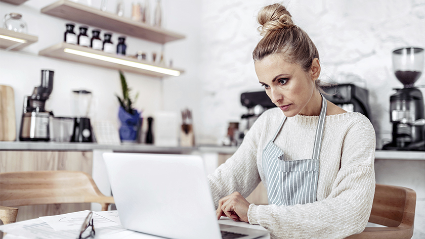 woman looking at laptop in her kitchen wearing an apron 