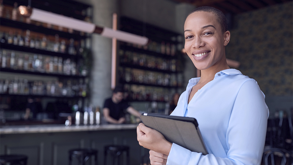 woman smiling holding a tablet in front of a bar