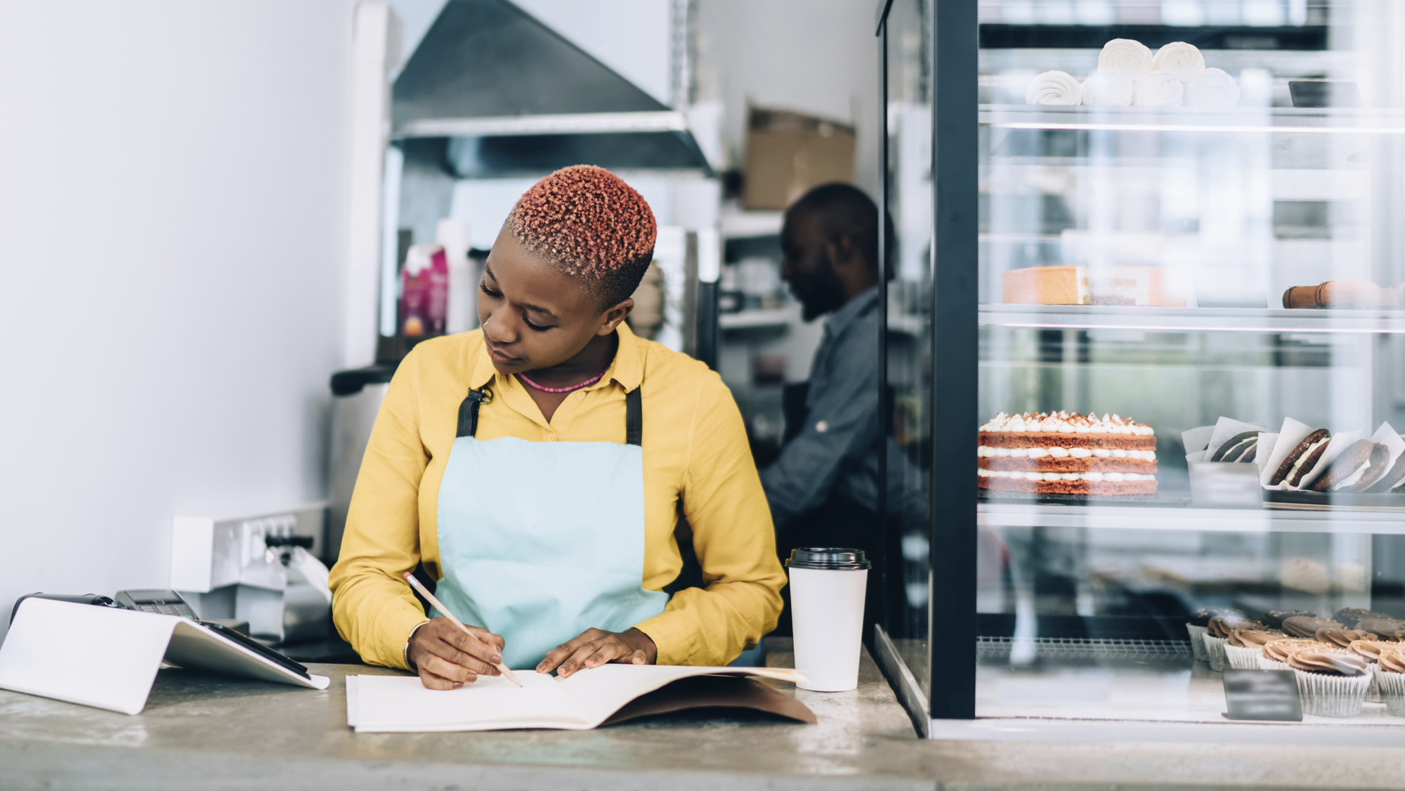 woman writing in notebook working at a bakery 