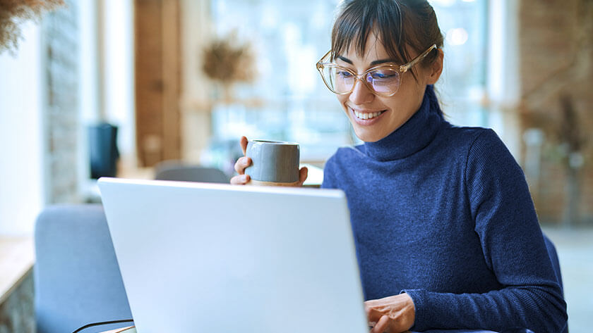 woman-smiling-drinking-coffee-looking-at-laptop  at home 