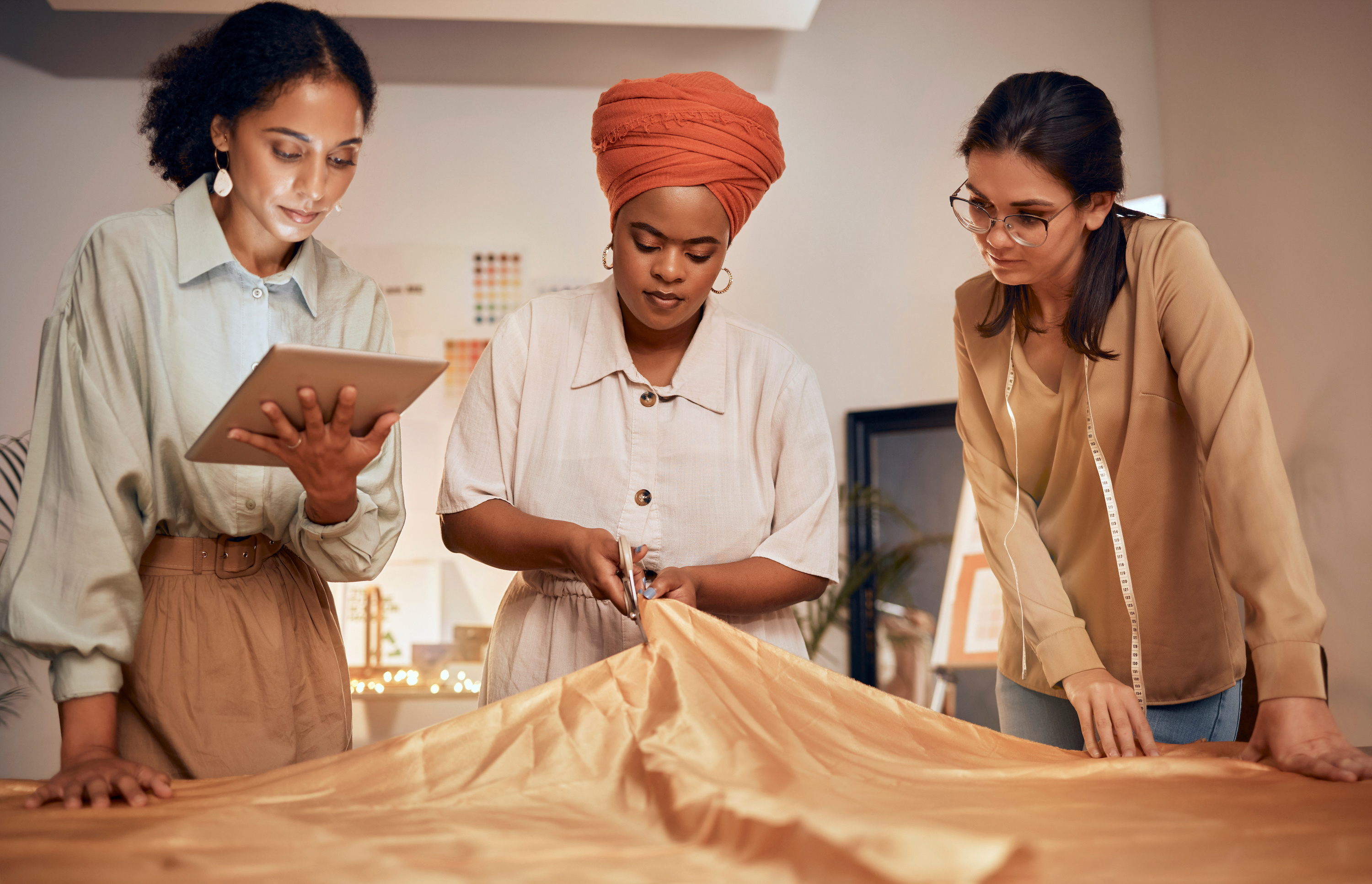 Three women gather around a table where one cuts a sheath of fabric. Learn the seven steps of forming an LLC.