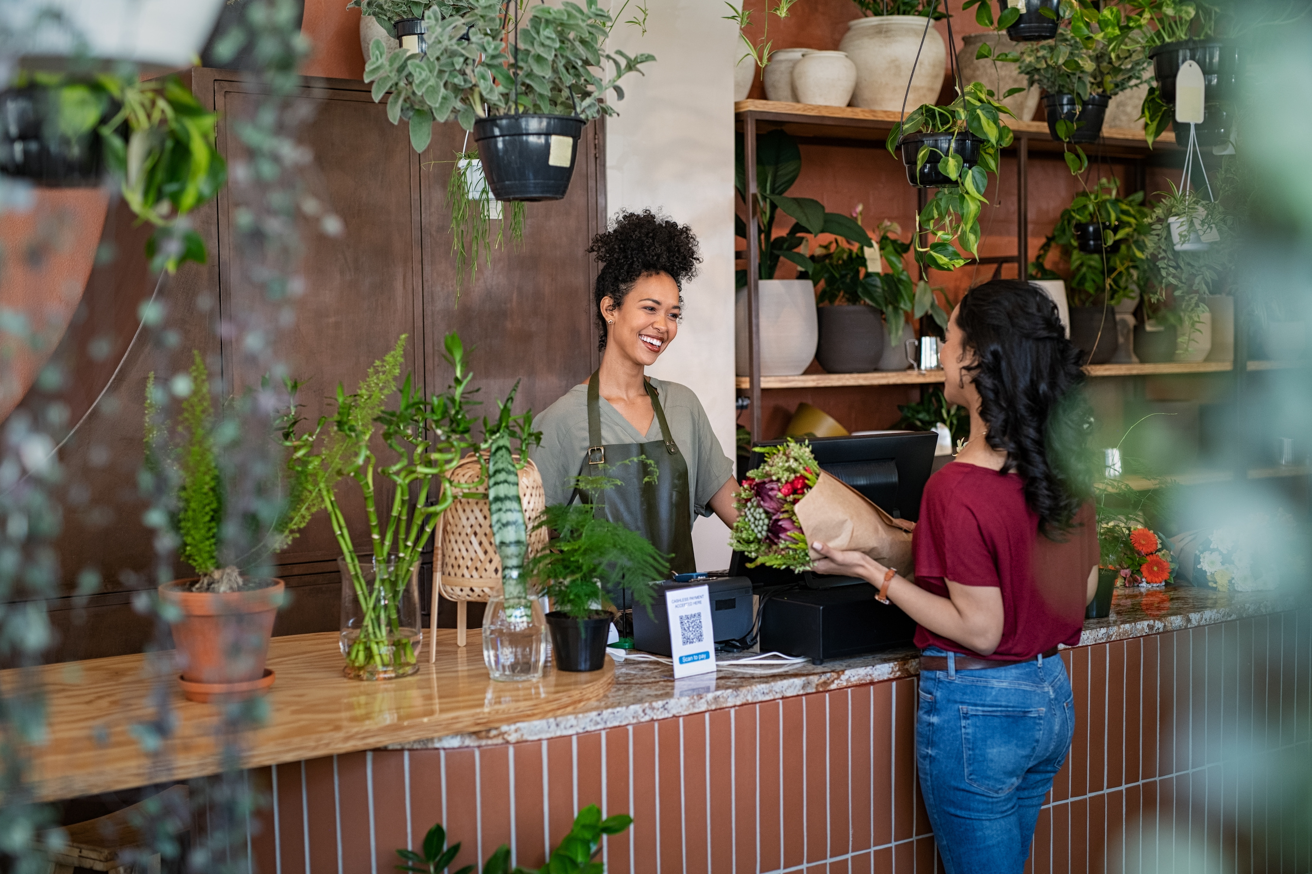 A woman at a counter hands a bouquet of flowers to a customer. The florist read how to form her LLC in seven steps when she started her business.