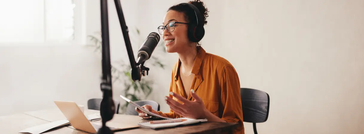 A woman in a brown shirt, sitting at her desk in her home studio talking into a microphone about how to register your DBA.