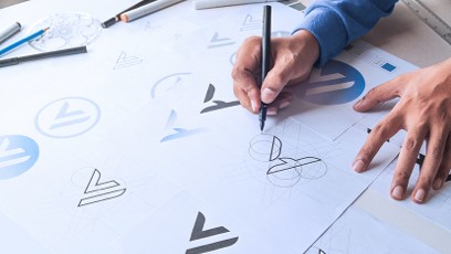 A designer holding a pen and sketching various logos.
