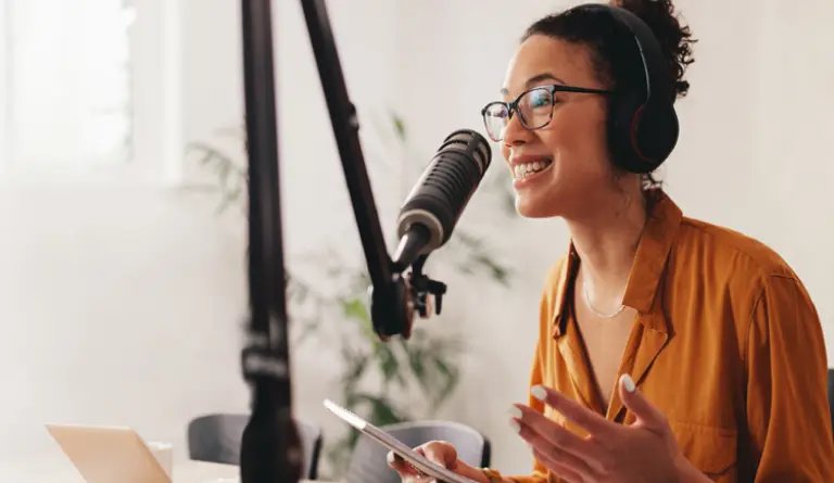 A woman in a brown shirt, sitting at her desk in her home studio talking into a microphone about how to register your DBA.