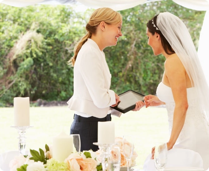 A female wedding planner reviewing proposal with bride at an outdoor wedding