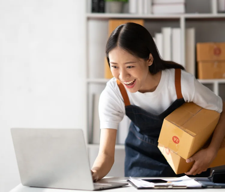Asian woman wearing a white t-shirt and a denim apron is smiling as she ships packages, because she formed her LLC with LegalZoom